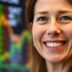 Cathie Wood smiling with a tech stock market background.