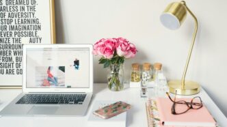 MacBook Air beside gold-colored study lamp and spiral books