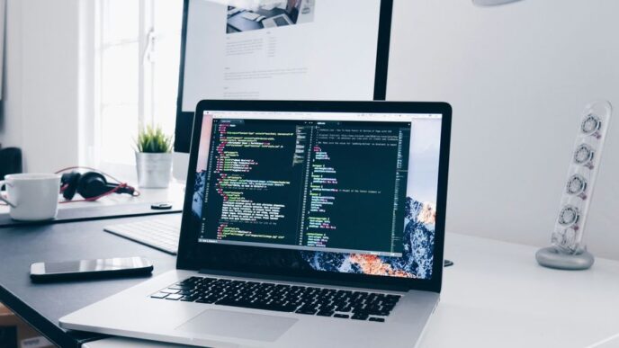 A MacBook with lines of code on its screen on a busy desk