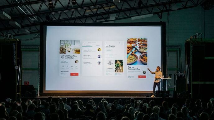 person discussing while standing in front of a large screen in front of people inside dim-lighted room