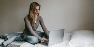 woman typing on MacBook Pro while sitting on bed in room