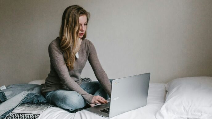 woman typing on MacBook Pro while sitting on bed in room