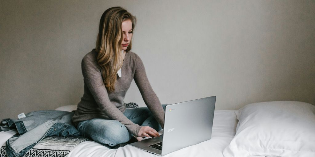 woman typing on MacBook Pro while sitting on bed in room