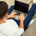 man wearing white sweatshirt using laptop computer sitting on sofa chair