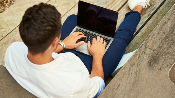 man wearing white sweatshirt using laptop computer sitting on sofa chair