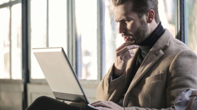 man holding his chin facing laptop computer
