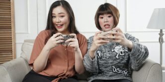two women holding controllers sitting on sofa chair
