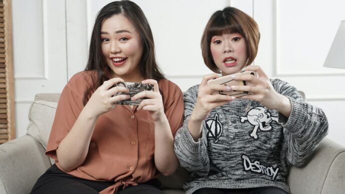 two women holding controllers sitting on sofa chair