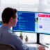 man in gray dress shirt sitting on chair in front of computer monitor