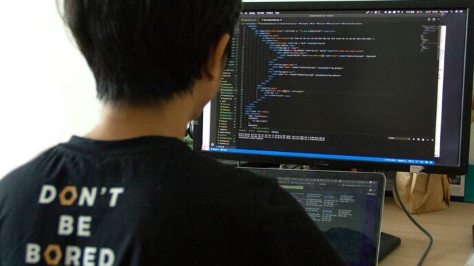 man in black shirt using laptop computer and flat screen monitor
