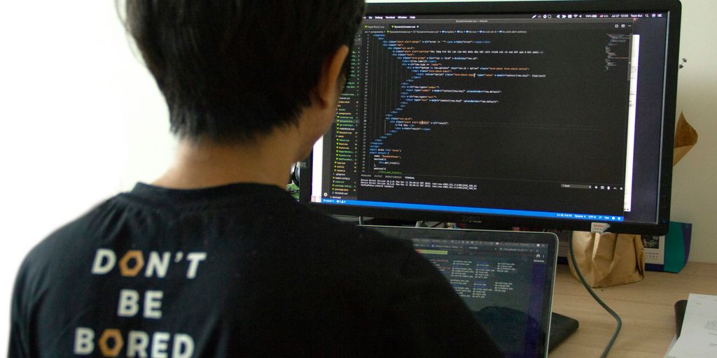 man in black shirt using laptop computer and flat screen monitor