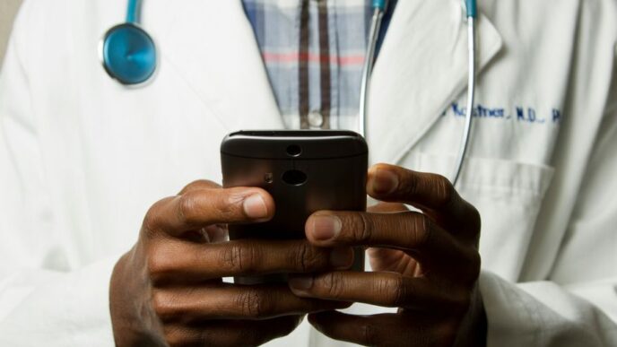 person wearing lavatory gown with green stethoscope on neck using phone while standing