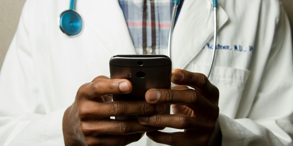 person wearing lavatory gown with green stethoscope on neck using phone while standing