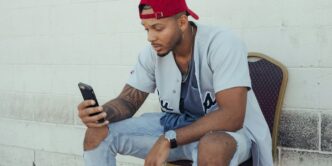 man in white polo shirt and red cap sitting on chair holding smartphone