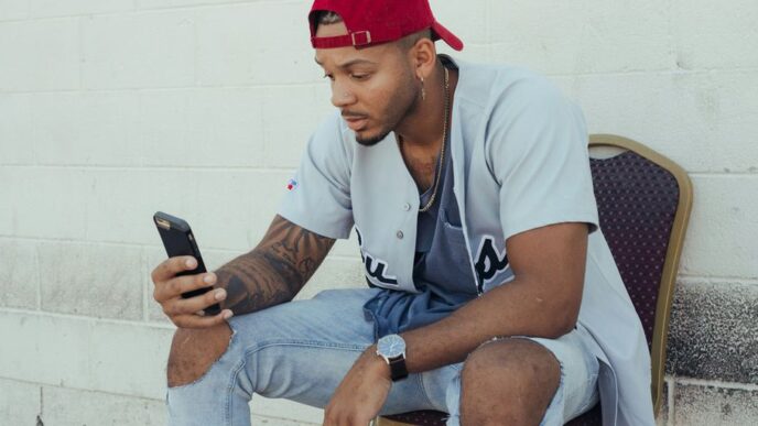 man in white polo shirt and red cap sitting on chair holding smartphone