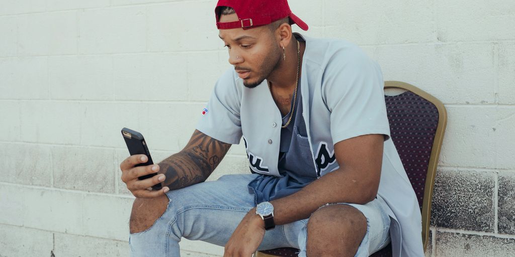 man in white polo shirt and red cap sitting on chair holding smartphone