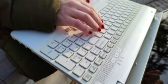 a woman is typing on a laptop outside