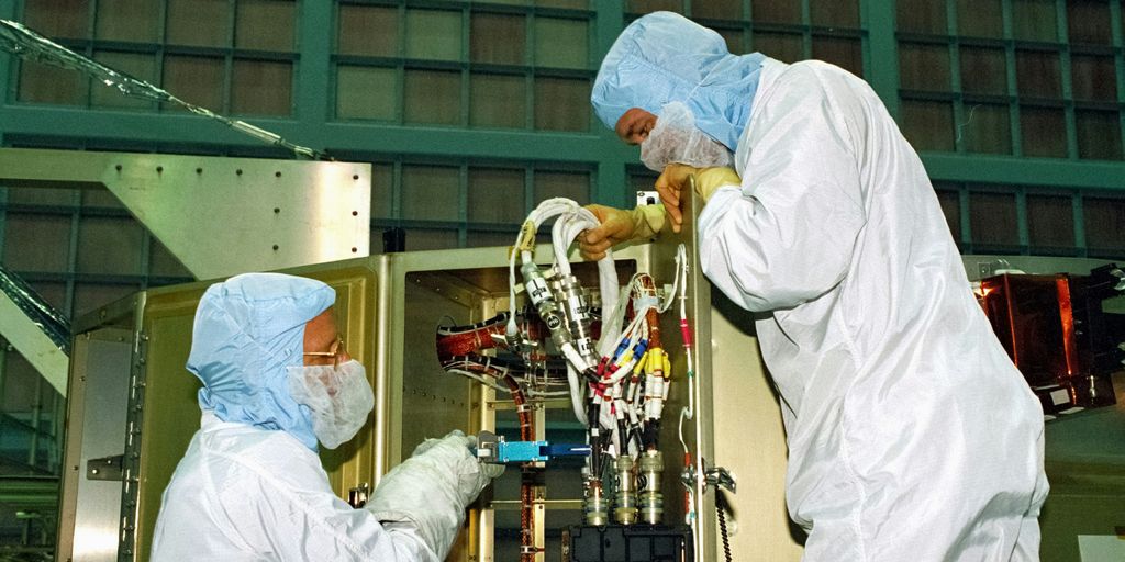 a couple of people in white suits working on a machine