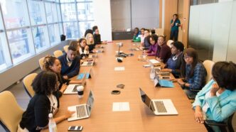 people sitting beside rectangular brown table with laptops