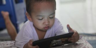 a small child laying on a bed playing with a tablet