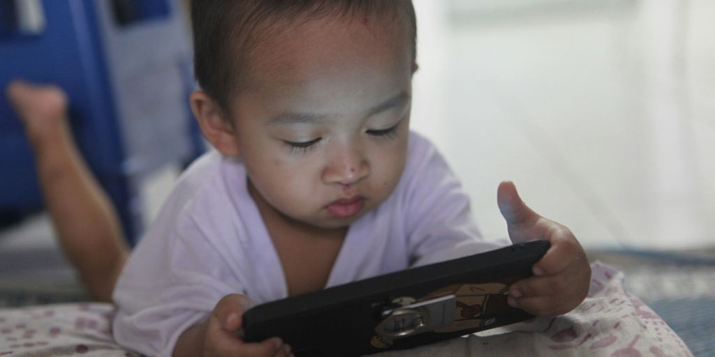 a small child laying on a bed playing with a tablet
