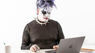a person in a cat mask sitting in front of a laptop