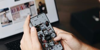 A person holding a cell phone in front of a laptop