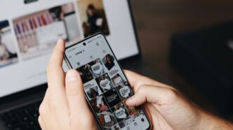 A person holding a cell phone in front of a laptop