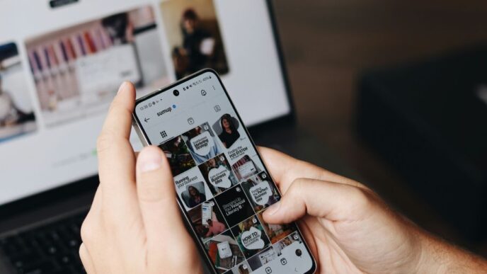 A person holding a cell phone in front of a laptop