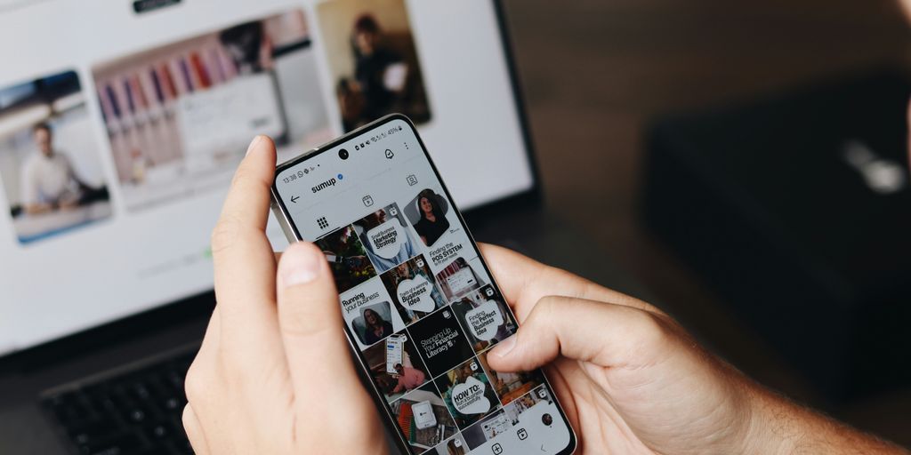 A person holding a cell phone in front of a laptop