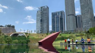 people near green field beside tall and high-rise building under blue and white skies