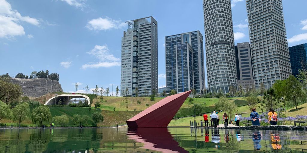 people near green field beside tall and high-rise building under blue and white skies