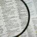 Magnifying glass focuses on a dictionary page.