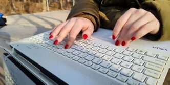 a woman with red nails typing on a white keyboard