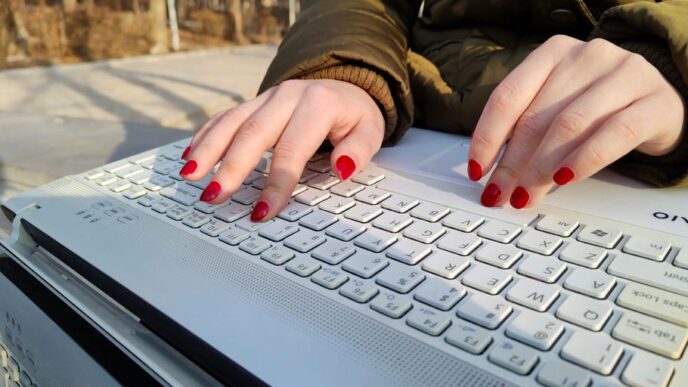 a woman with red nails typing on a white keyboard