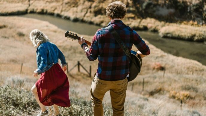 man playing guitar standing behind woman on mountain