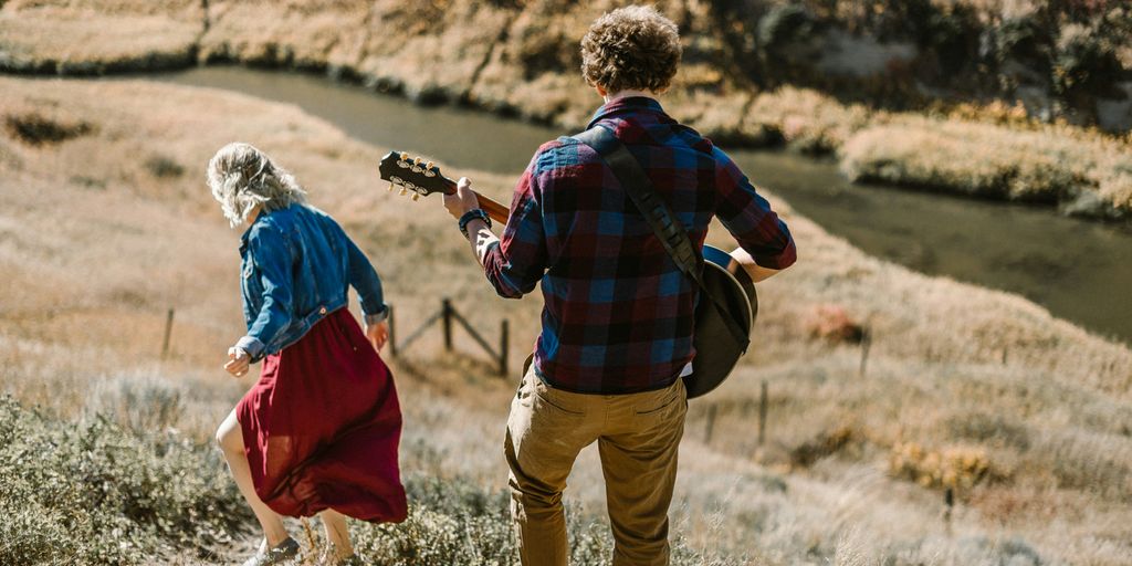 man playing guitar standing behind woman on mountain