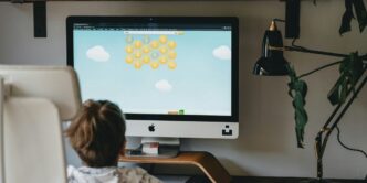 girl in white and blue floral shirt sitting on chair in front of silver imac