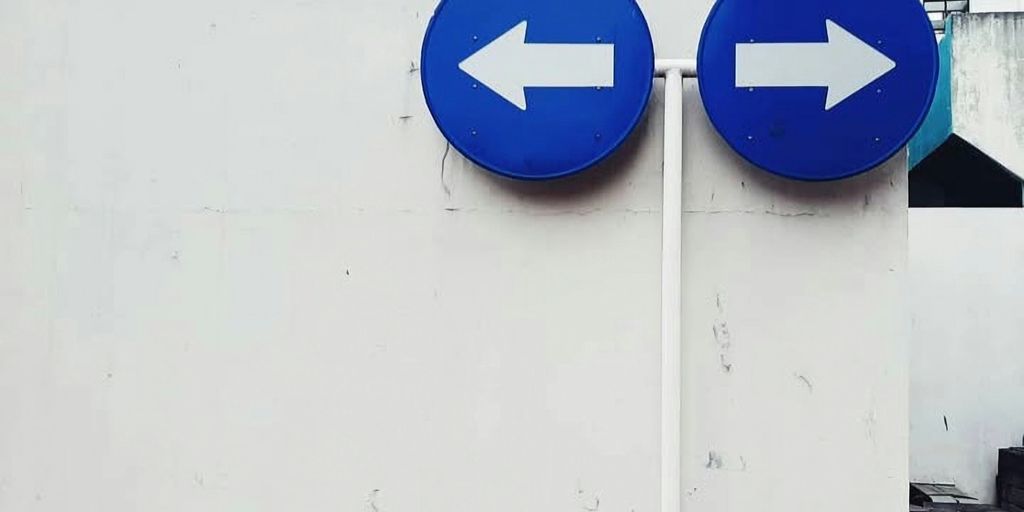 Two blue signs pointing in opposite directions on a white wall