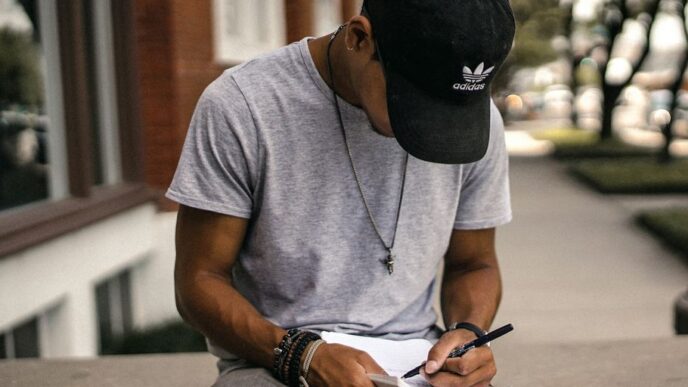 person in black adidas cap sitting on bench writing on notebook