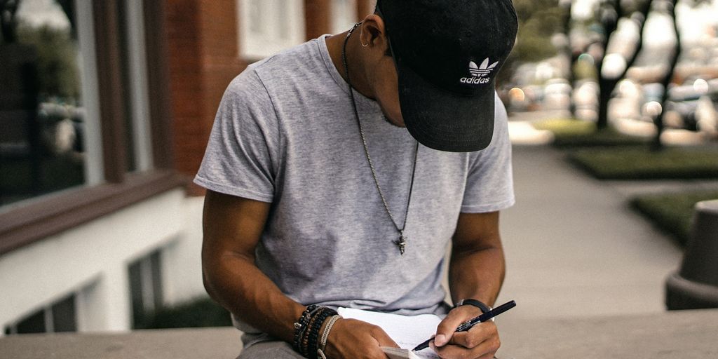 person in black adidas cap sitting on bench writing on notebook