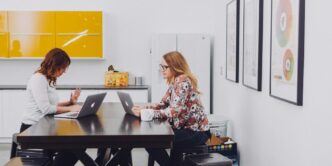 2 women using laptop by table