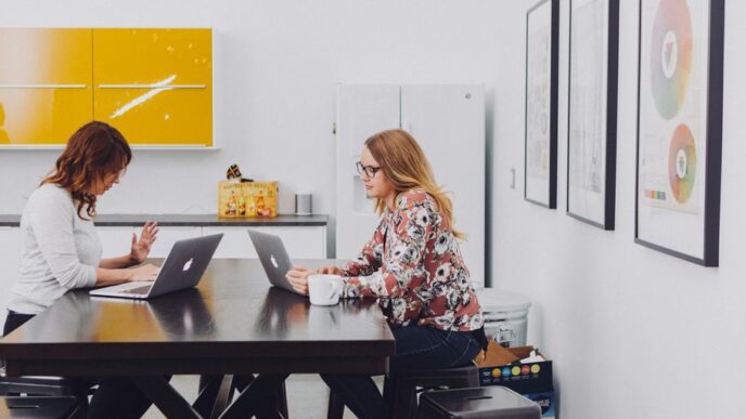 2 women using laptop by table