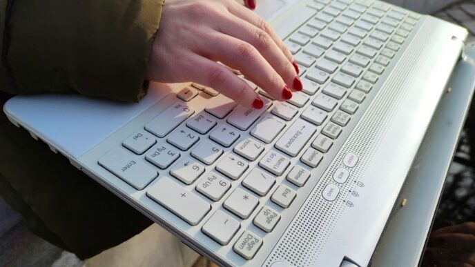 a woman is typing on a laptop outside