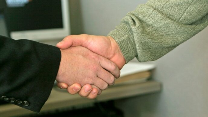 two people shaking hands in front of a computer monitor