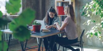 Two women collaborate at a desk in an office.