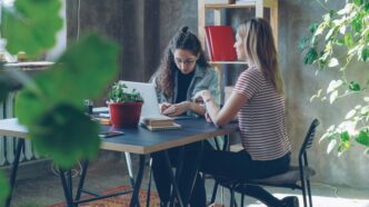 Two women collaborate at a desk in an office.