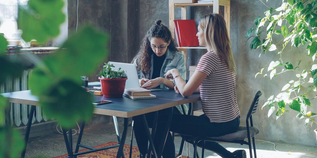 Two women collaborate at a desk in an office.