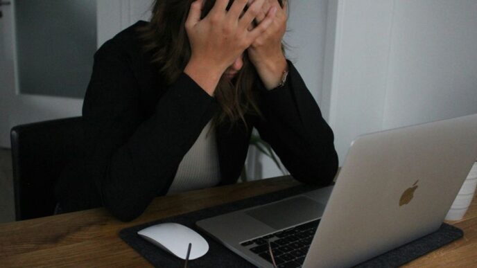 a woman covering her face while looking at a laptop