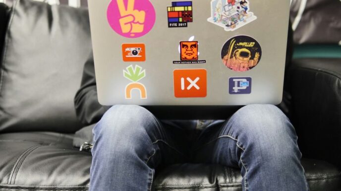 man using silver MacBook sitting on black leather sofa